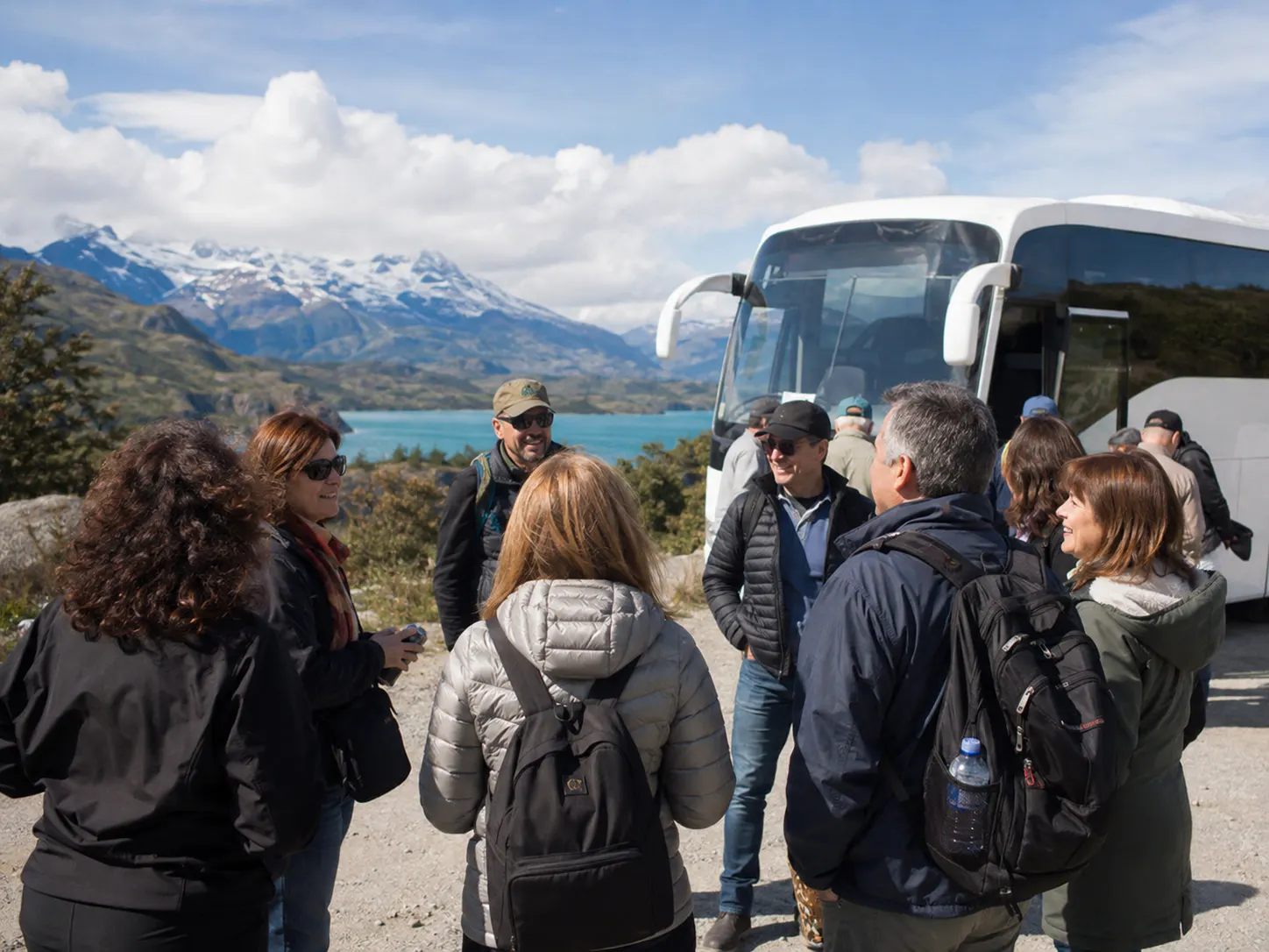 Grupo de viajeros con mochilas junto a un autobús turístico en una zona de lagos